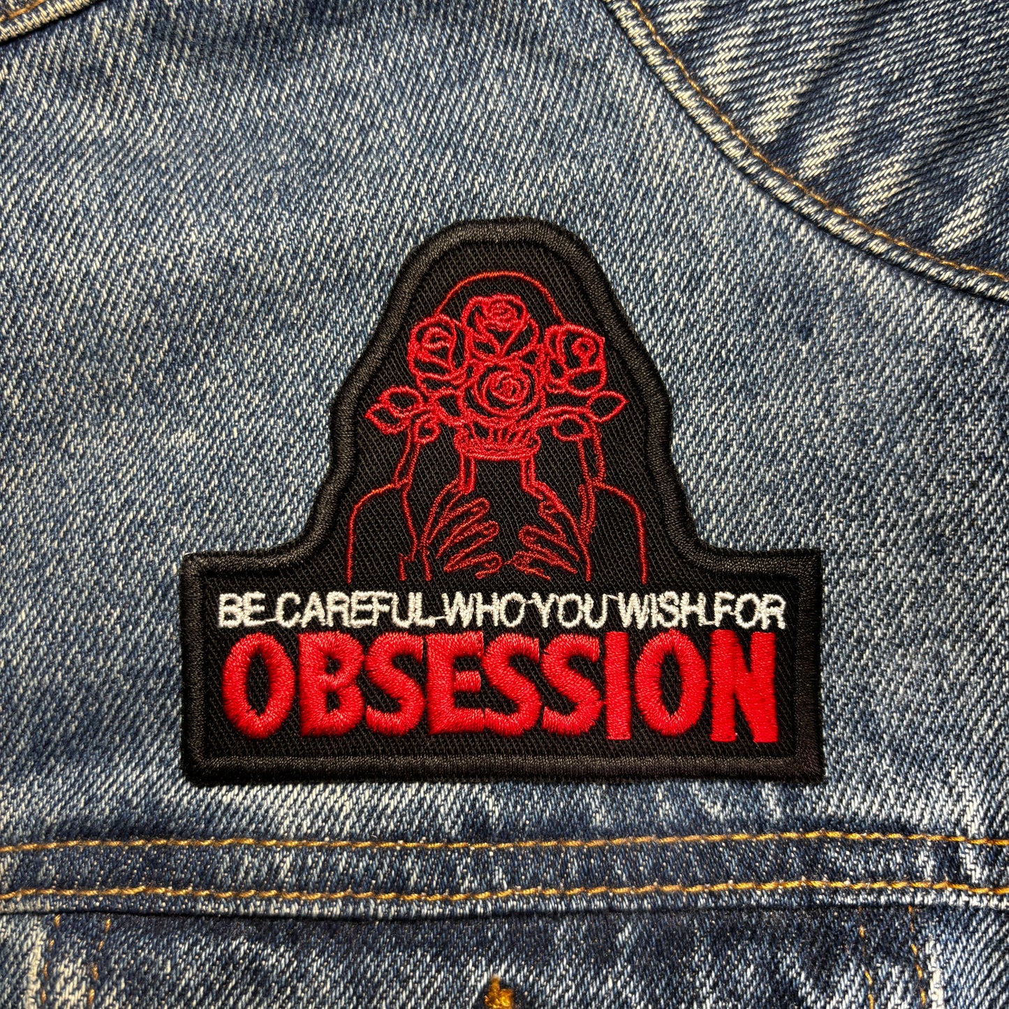 Patch with 'Be careful who you wish for obsession' text on a denim jacket.