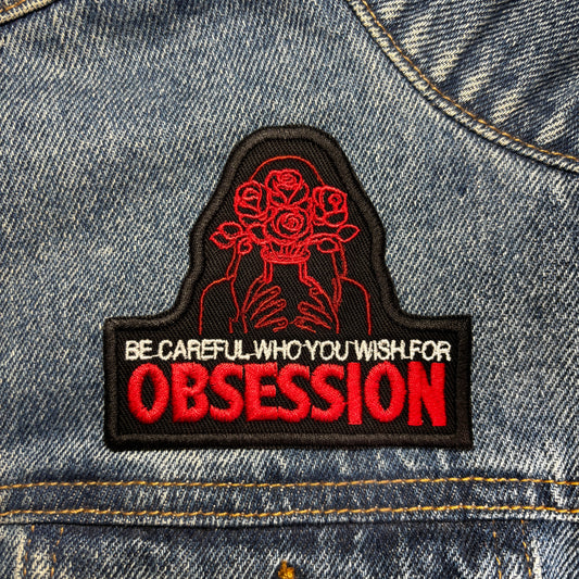 Patch with 'Be careful who you wish for obsession' text on a denim jacket.